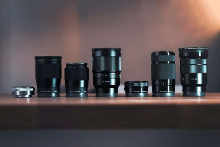 Lineup of Sony E-mount camera lenses arranged on a wooden table, including SIGMA 18-50mm F2.8, FE 35mm F1.4, and E 18-105mm F4 G
